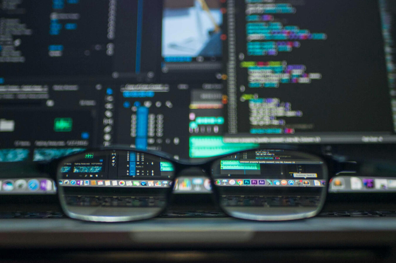 A pair of glasses sits in front of a computer screen with code on if