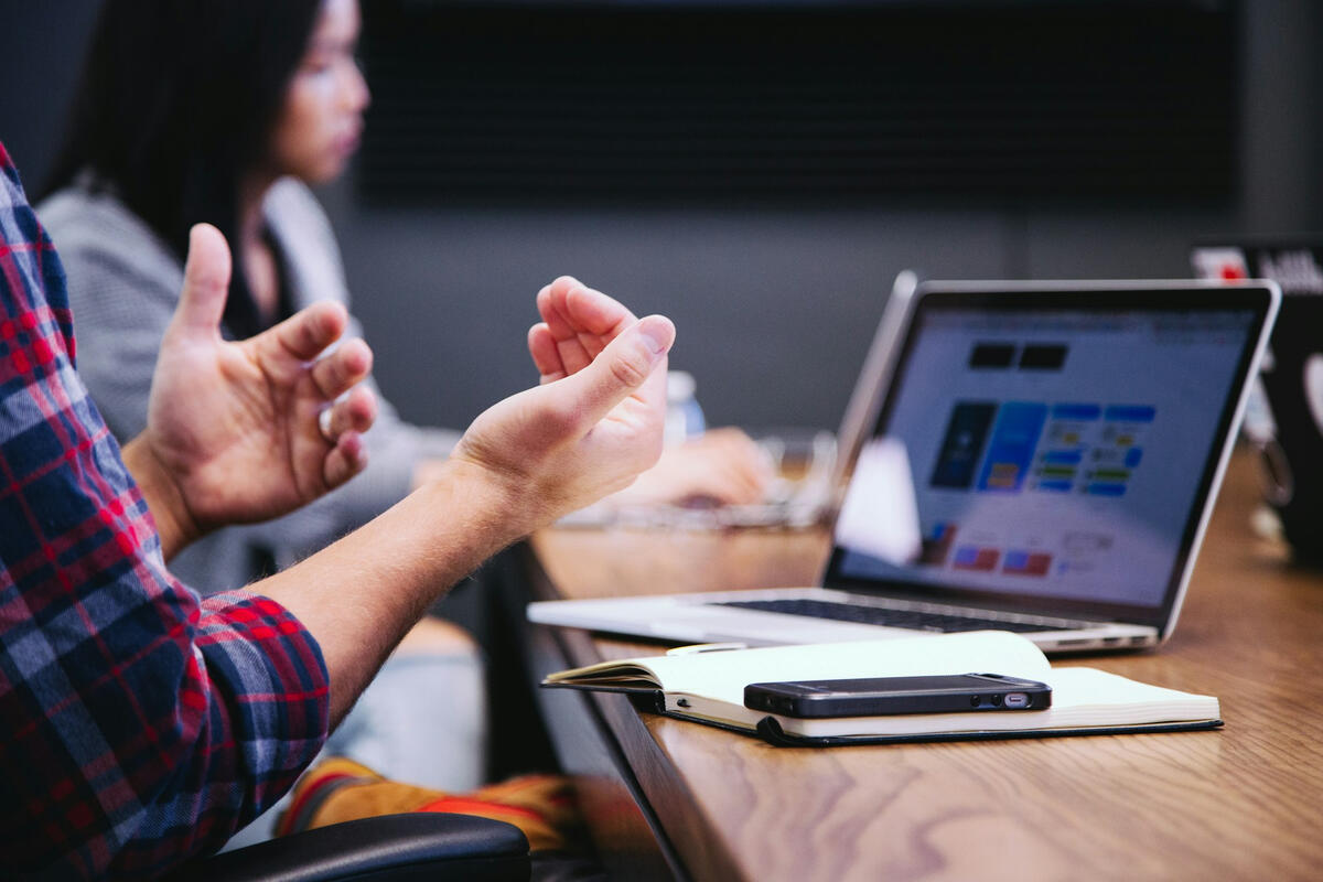 A man gestures in front of a laptop during a business meeting
